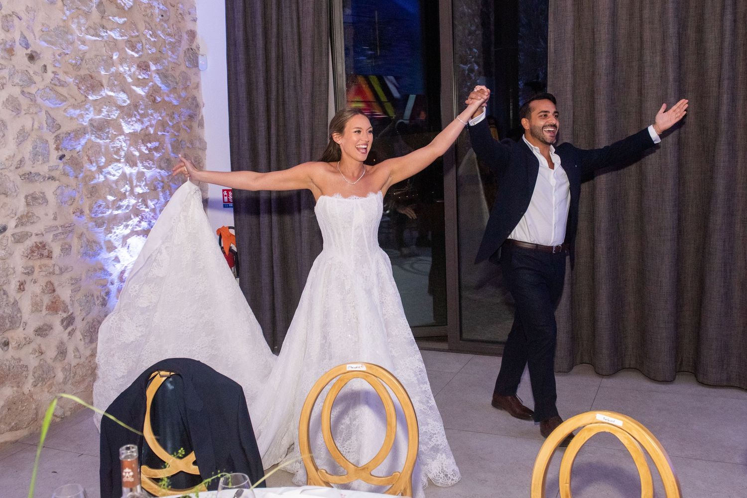 A wedding couple and guests dance and celebrate in an elegant stone-walled reception venue.