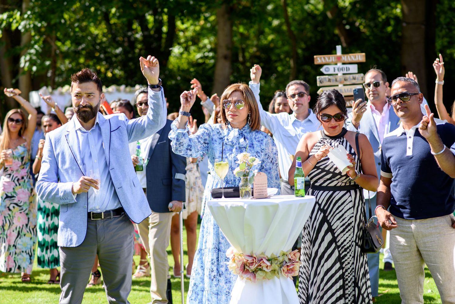 A group of wedding guests dance and celebrate on an outdoor dance floor during a daytime reception.