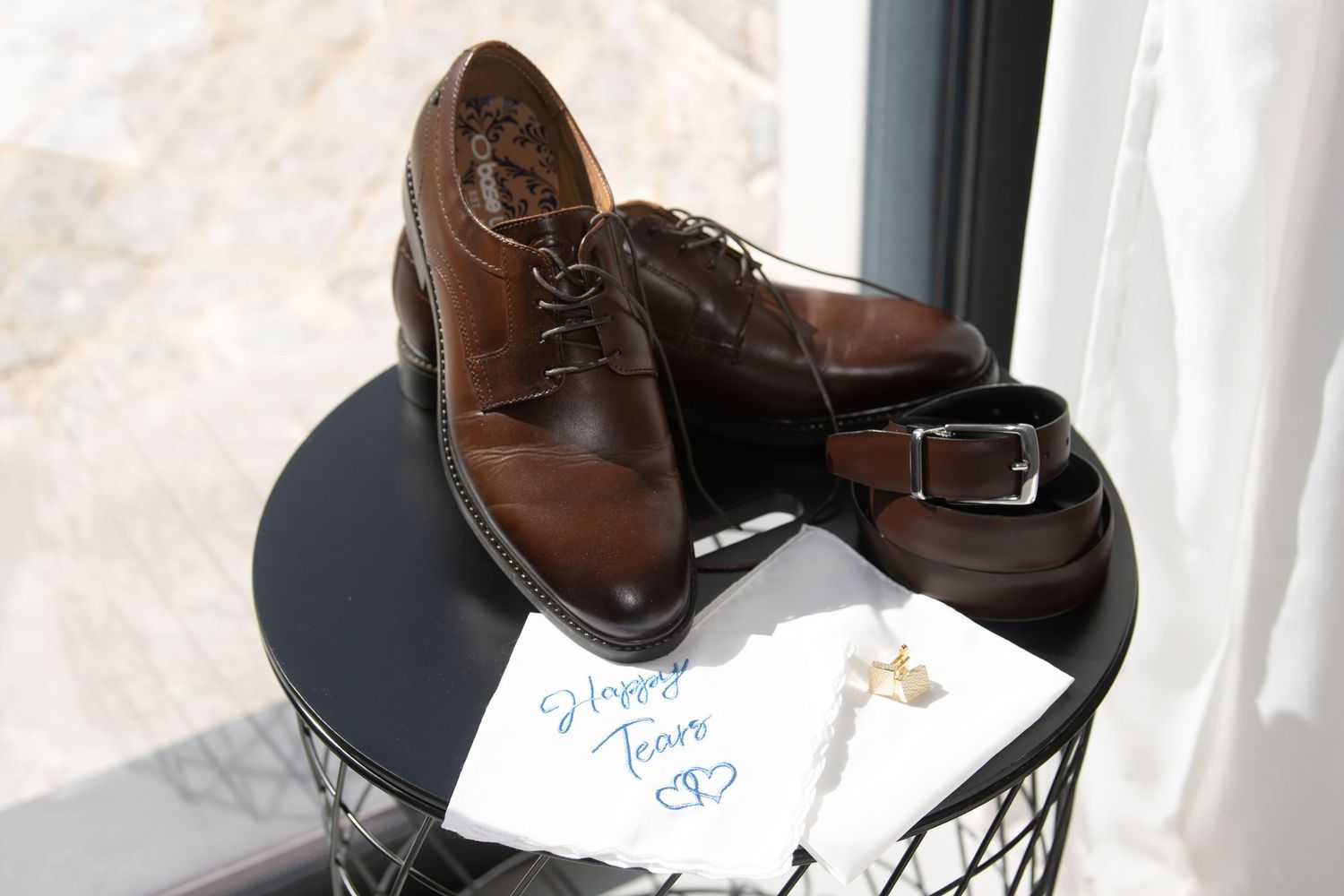 Brown leather dress shoes and a belt displayed on a black round side table with white paper.