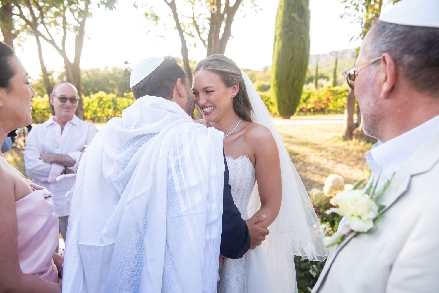 A joyful outdoor wedding ceremony takes place among cypress trees during golden hour.