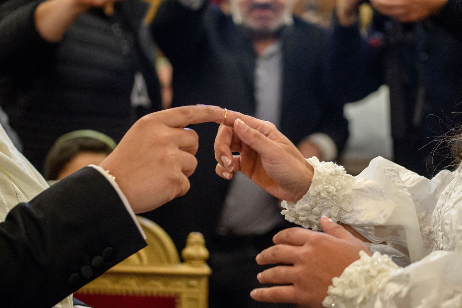Close-up of hands exchanging wedding rings during a traditional ceremony with guests in background.