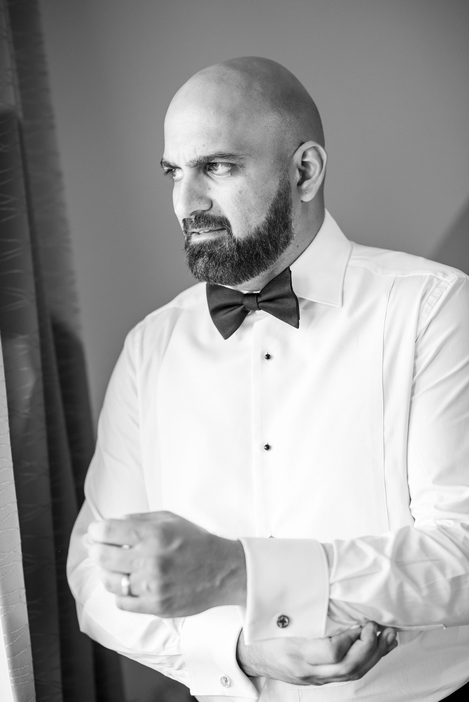 Man in white dress shirt and black bow tie adjusts his cuffs in black and white photo series.