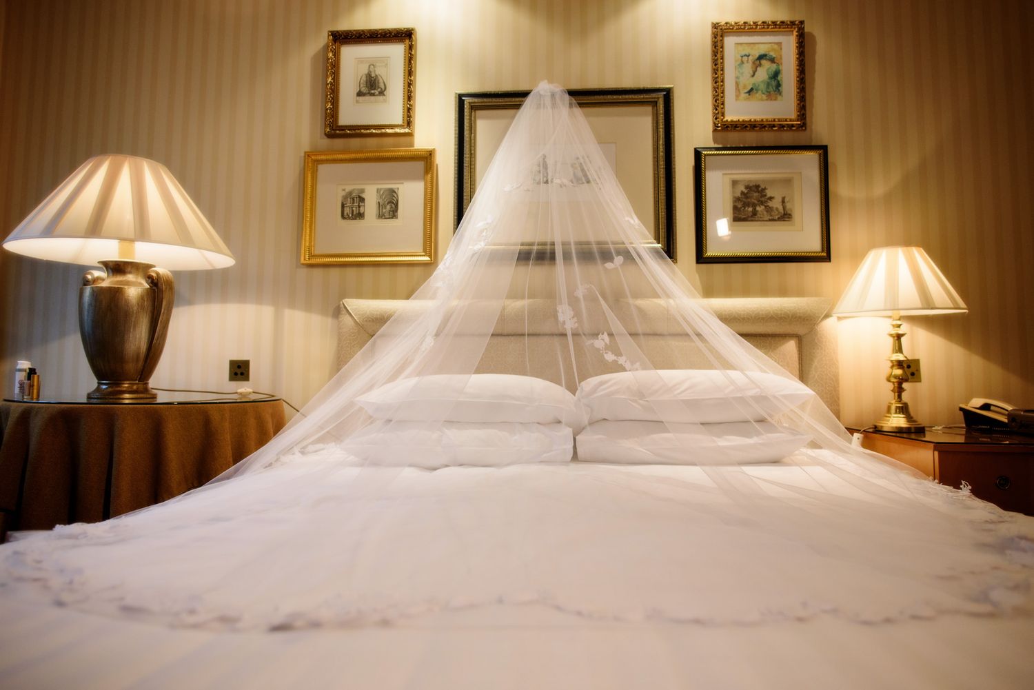 Elegant bedroom interior with white mosquito net canopy over bed, framed artwork, and matching table lamps.