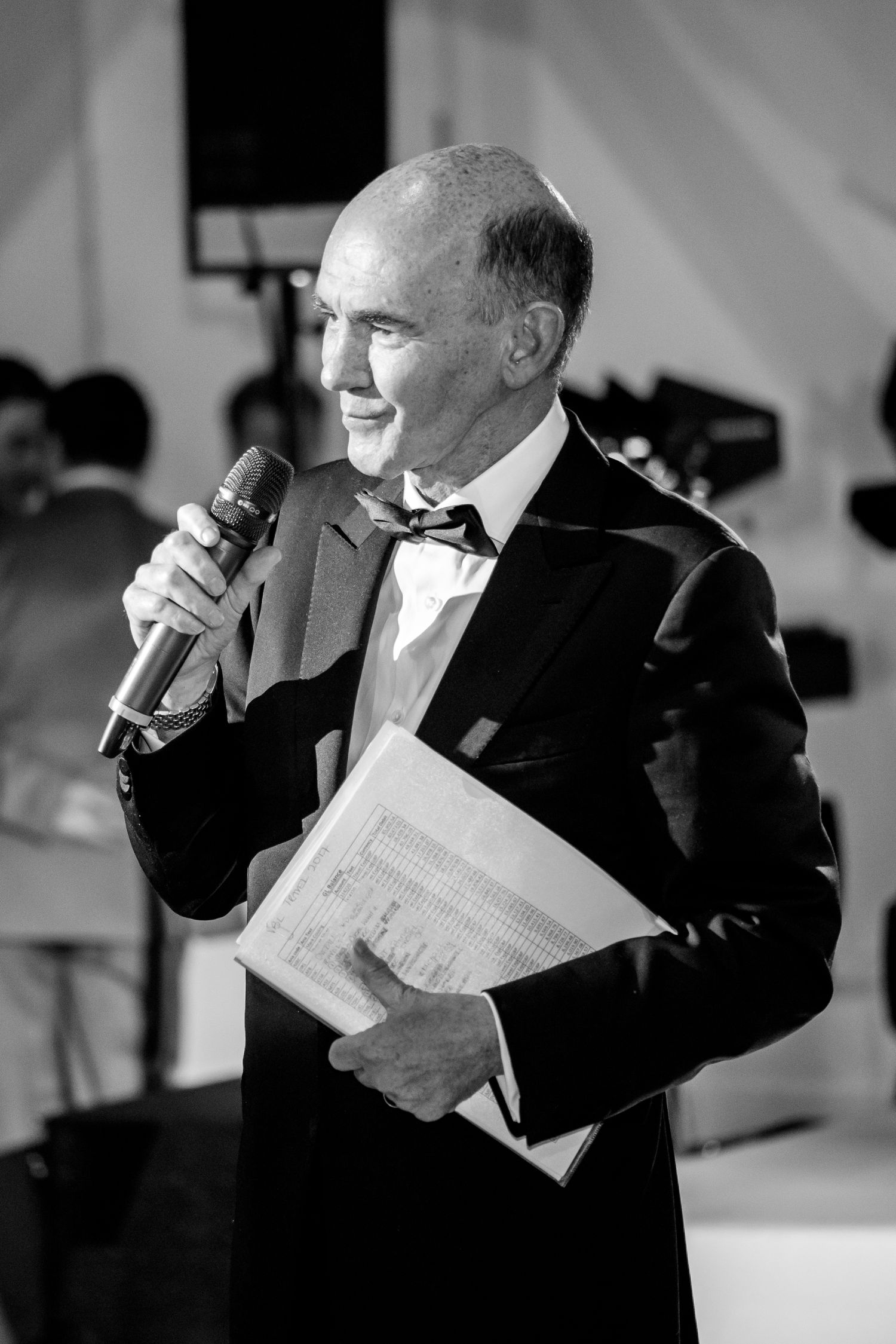 Black and white photo of speaker holding papers at formal event.