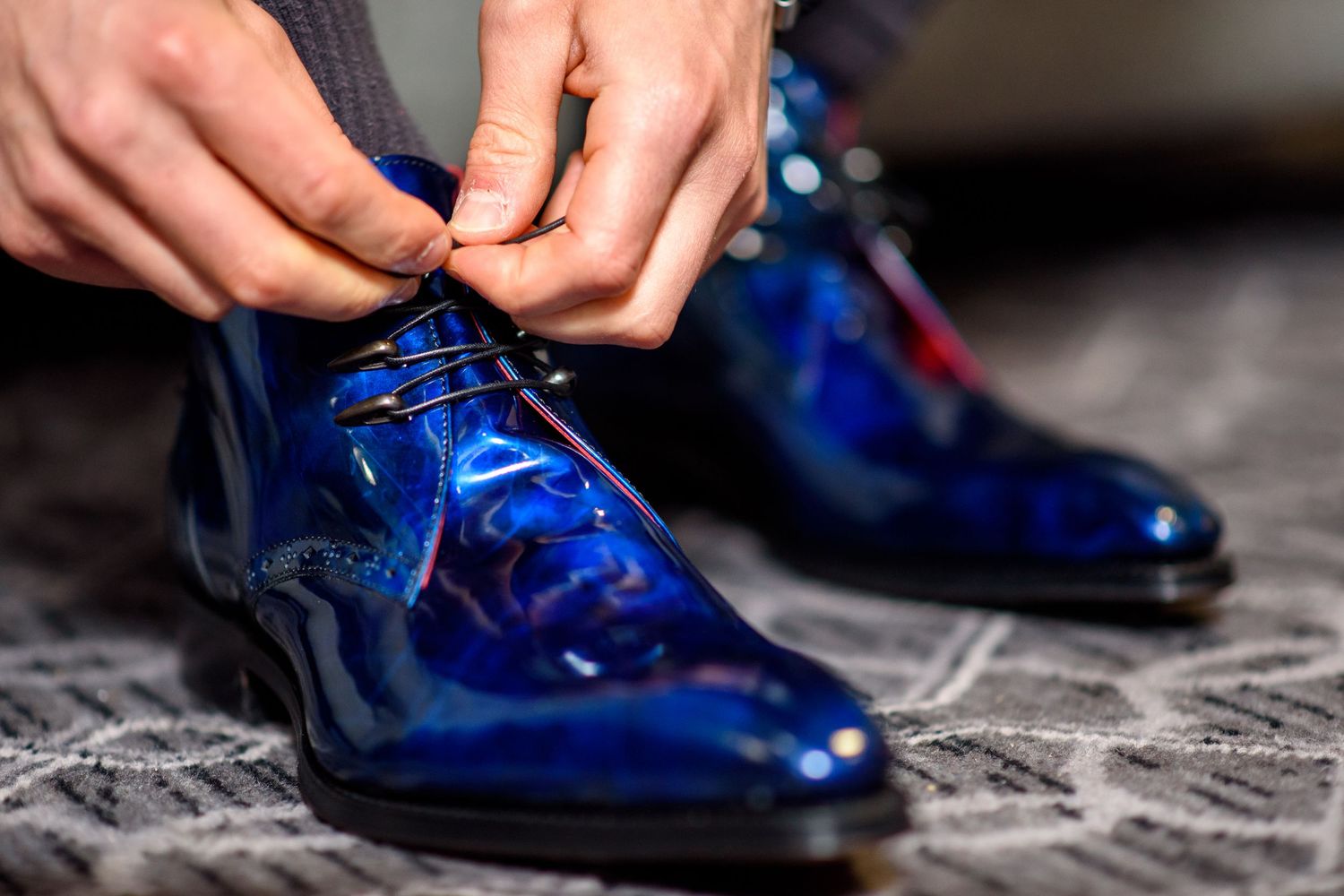 Close-up sequence showing someone tying bright blue patent leather dress shoes on a textured gray surface.