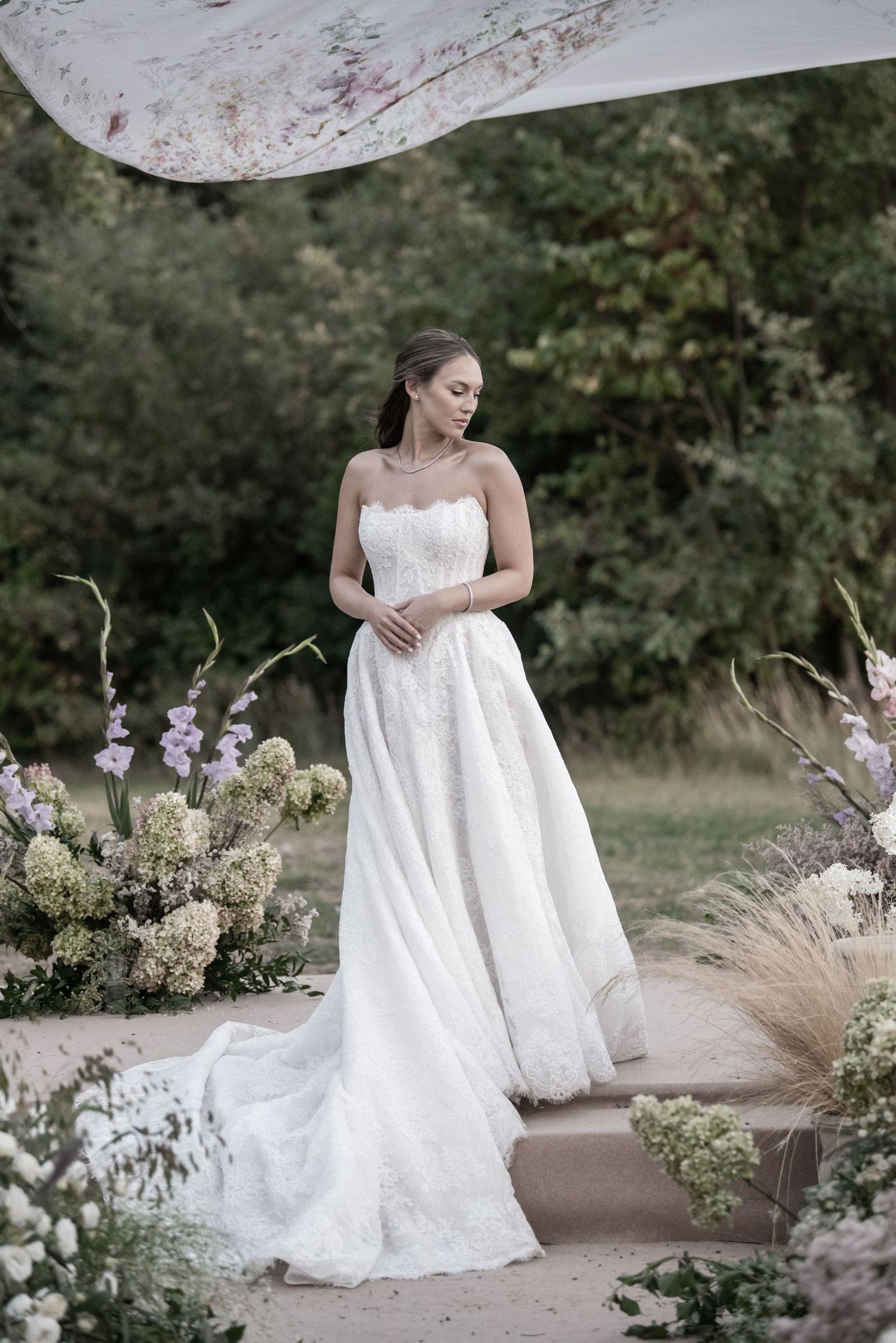 A romantic outdoor bridal portrait session featuring a white lace gown and natural garden backdrop with purple flowers.