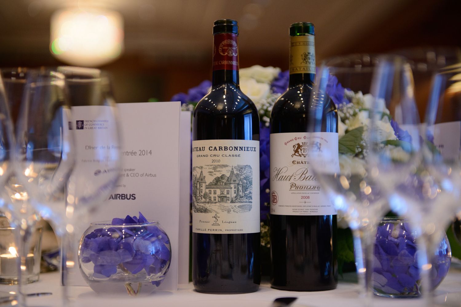 Wine bottles and glasses arranged on formal dining table with blue floral accents.