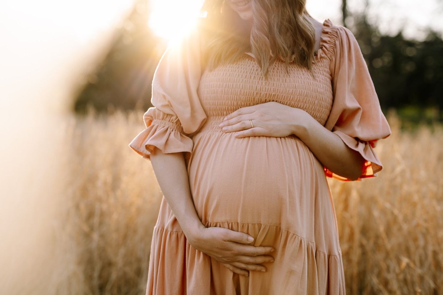 Pregnant woman cradles her belly and looks down with golden light around her