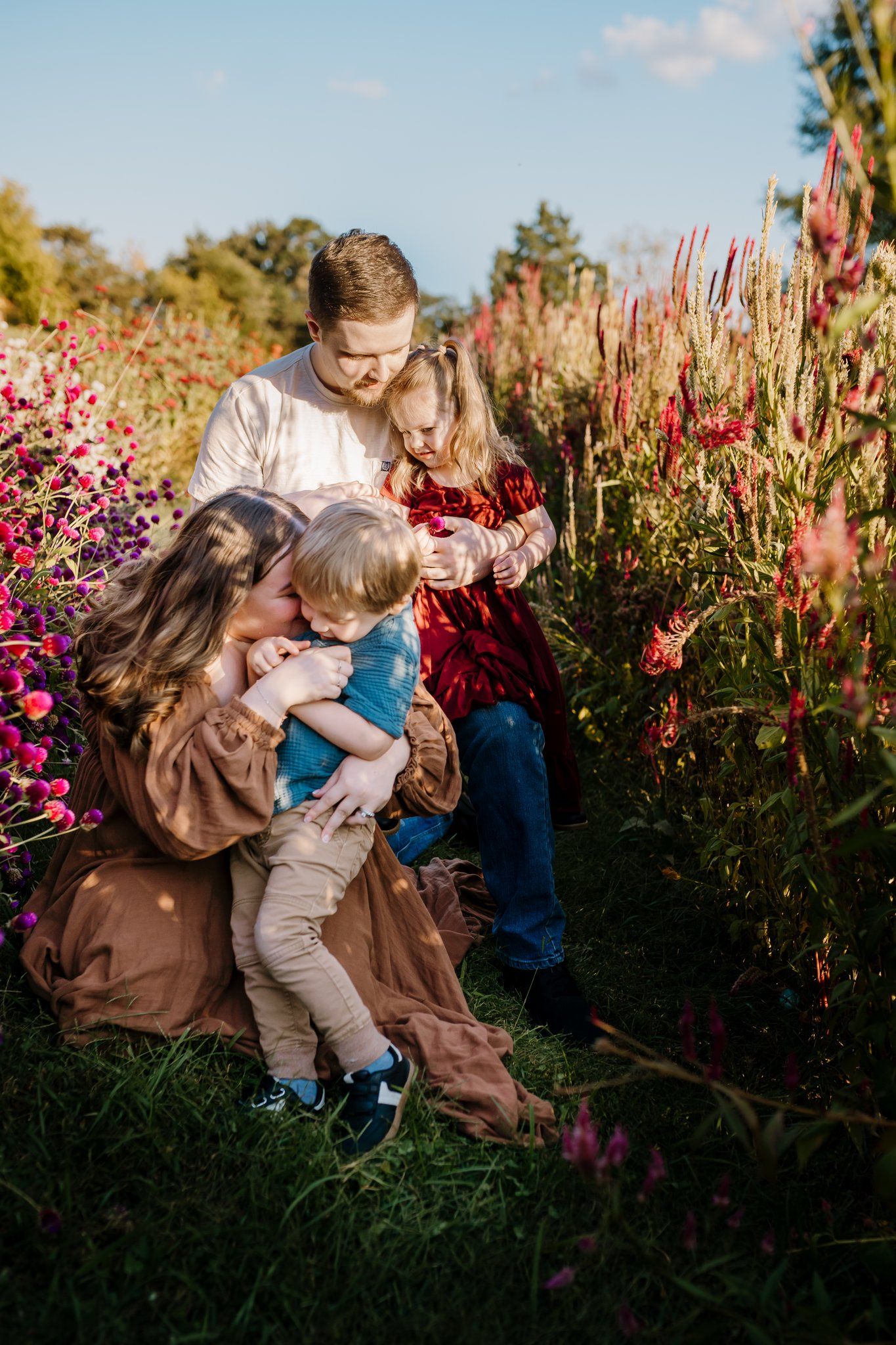Parents crouch in a flower field snuggling and tickling their two toddlers