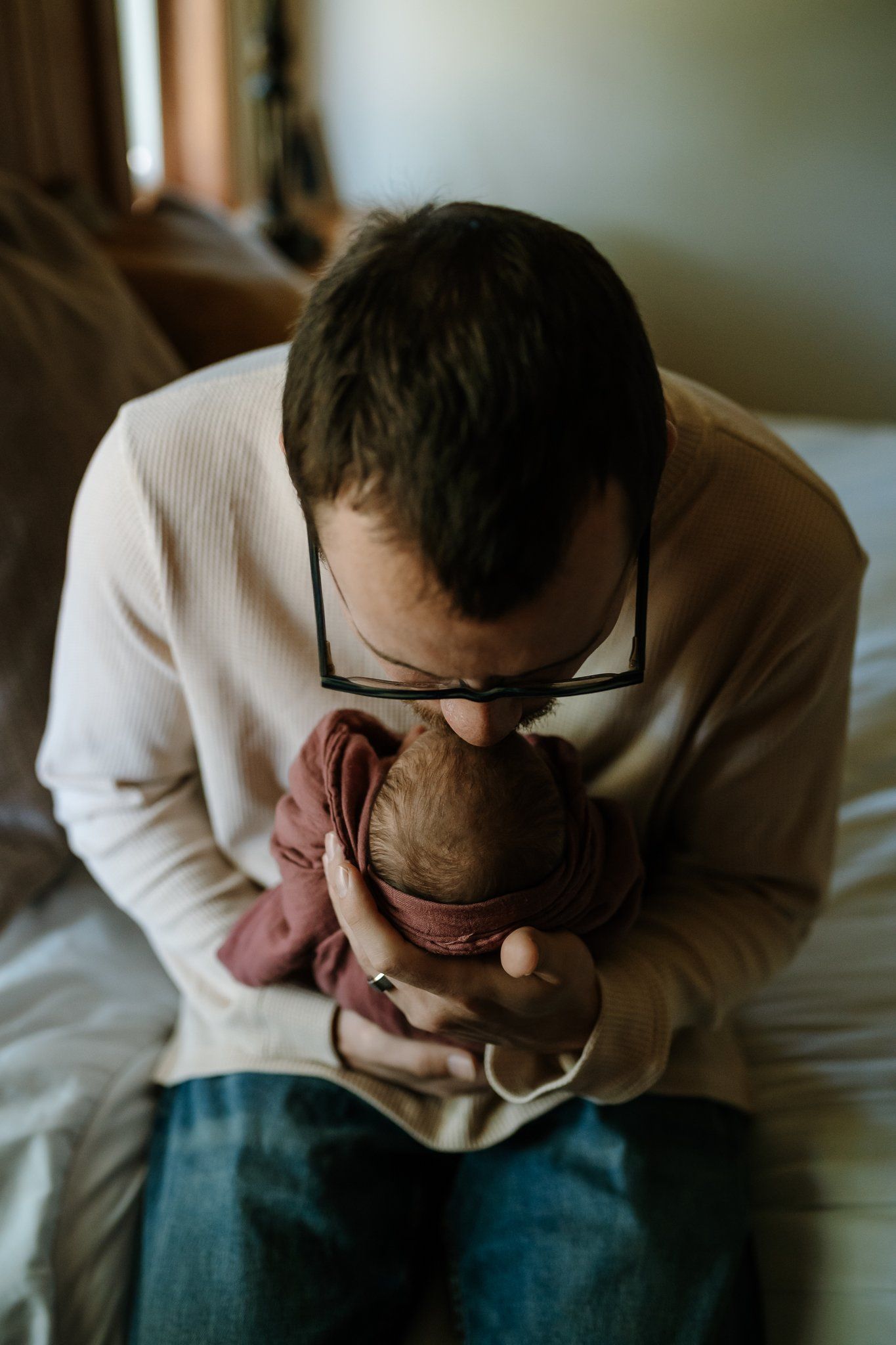 Dad sits on his bed and kisses newborn daughter