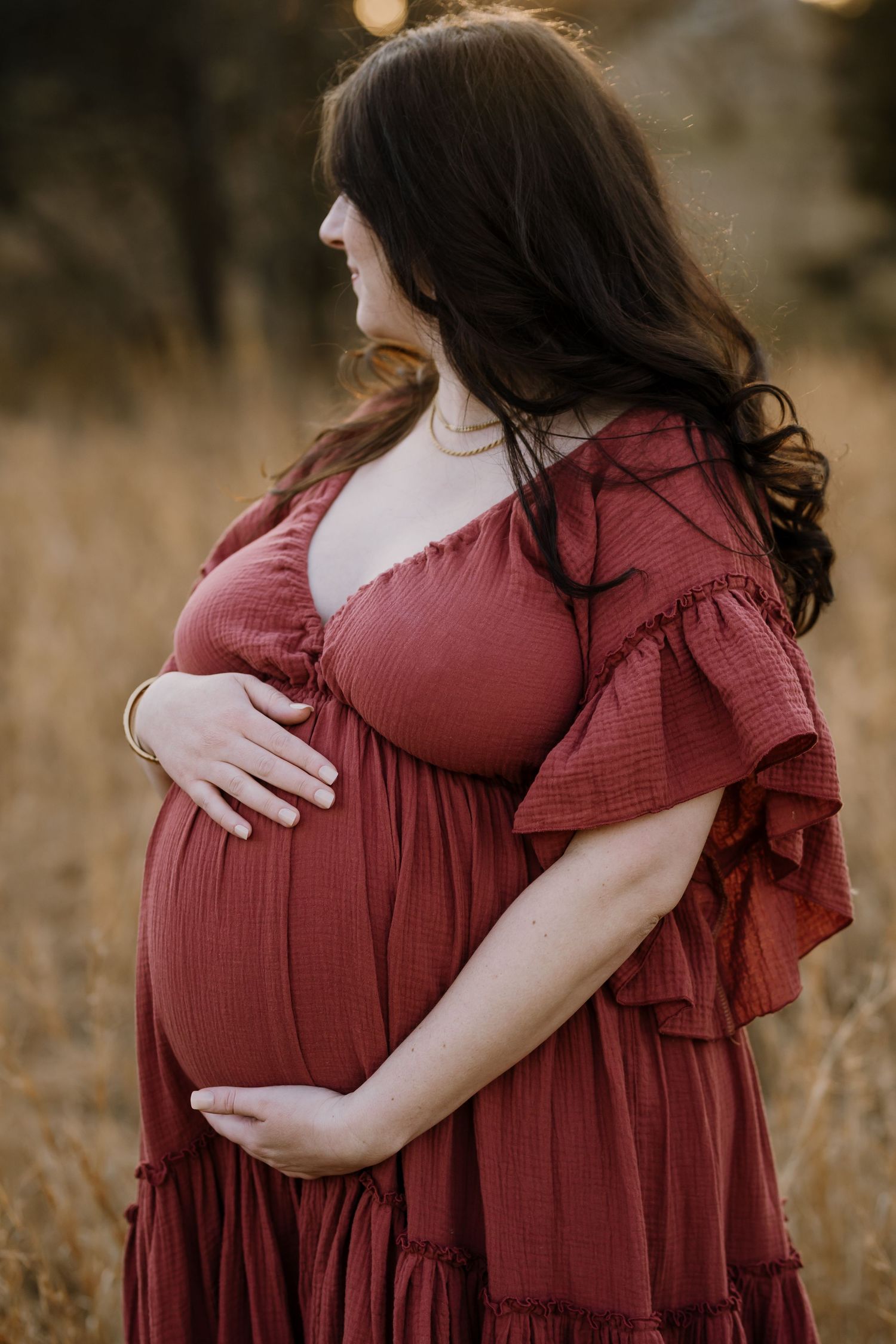 Woman cradles her pregnant belly during maternity photos and looks away from the camera