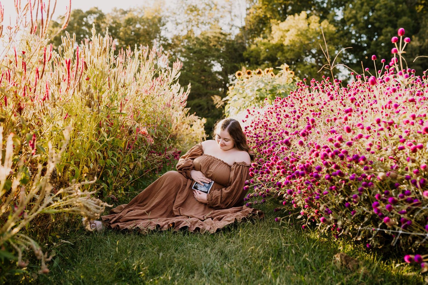 Woman sits with ultrasound picture in a flower field