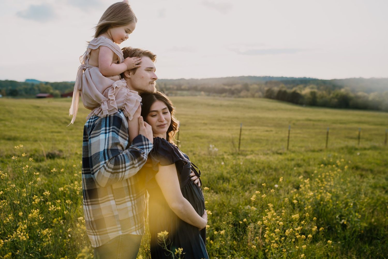 Young family stands together in a mustard field during maternity photo shoot