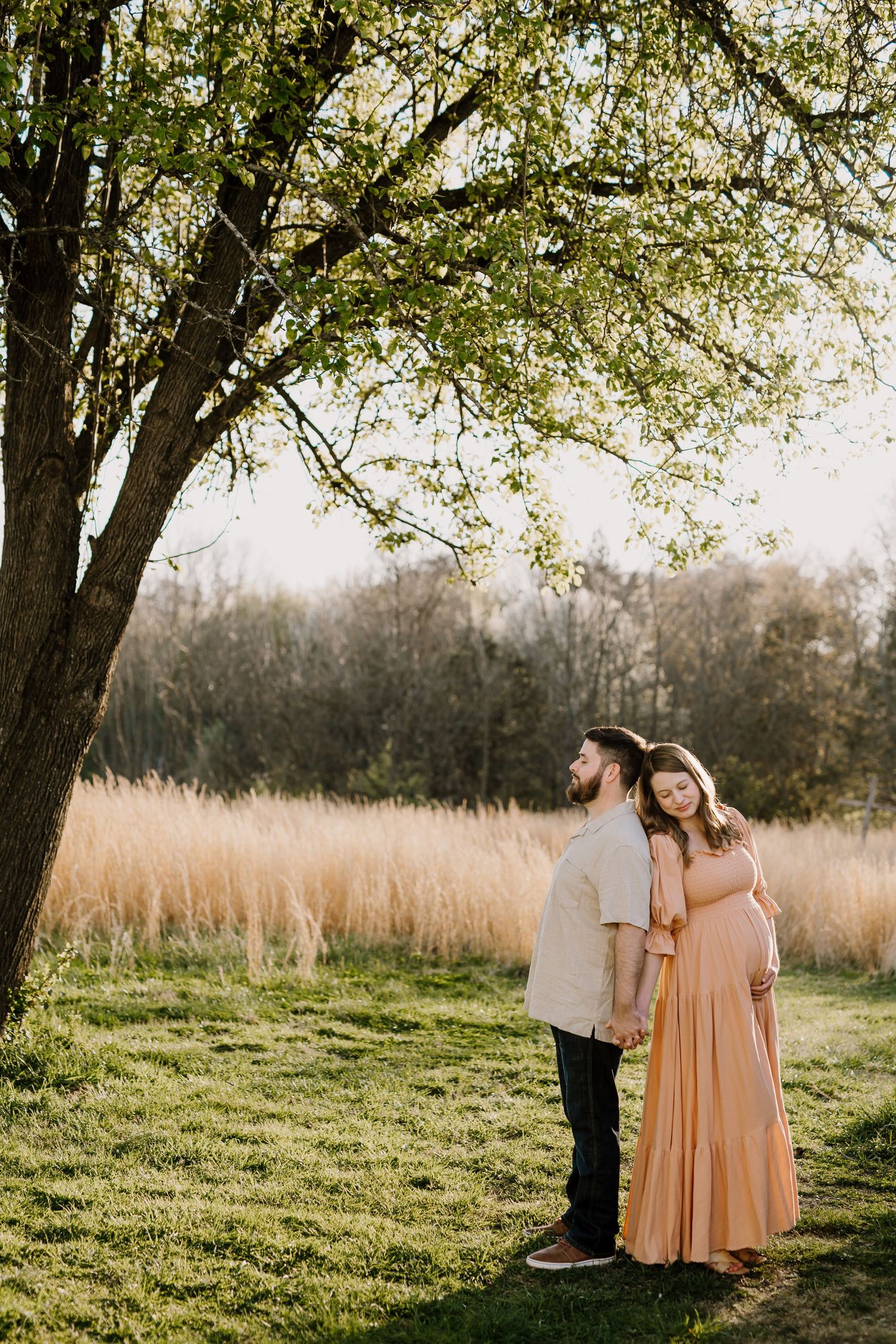 Pregnant woman stands with husband under a tree in knoxville during maternity pictures