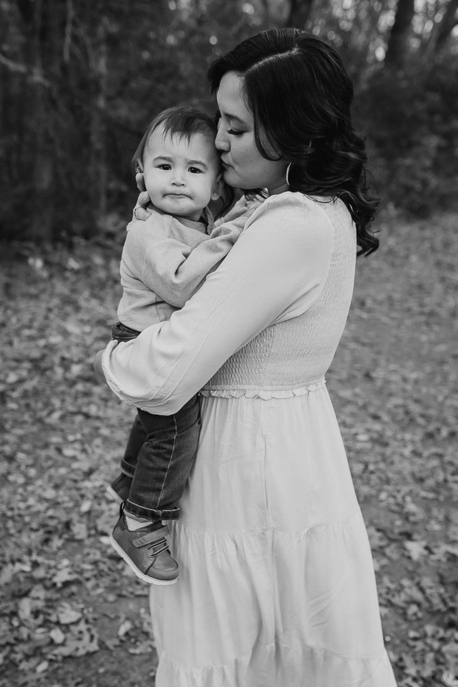toddler looks at camera and makes a funny face as his mom hugs him and kisses him