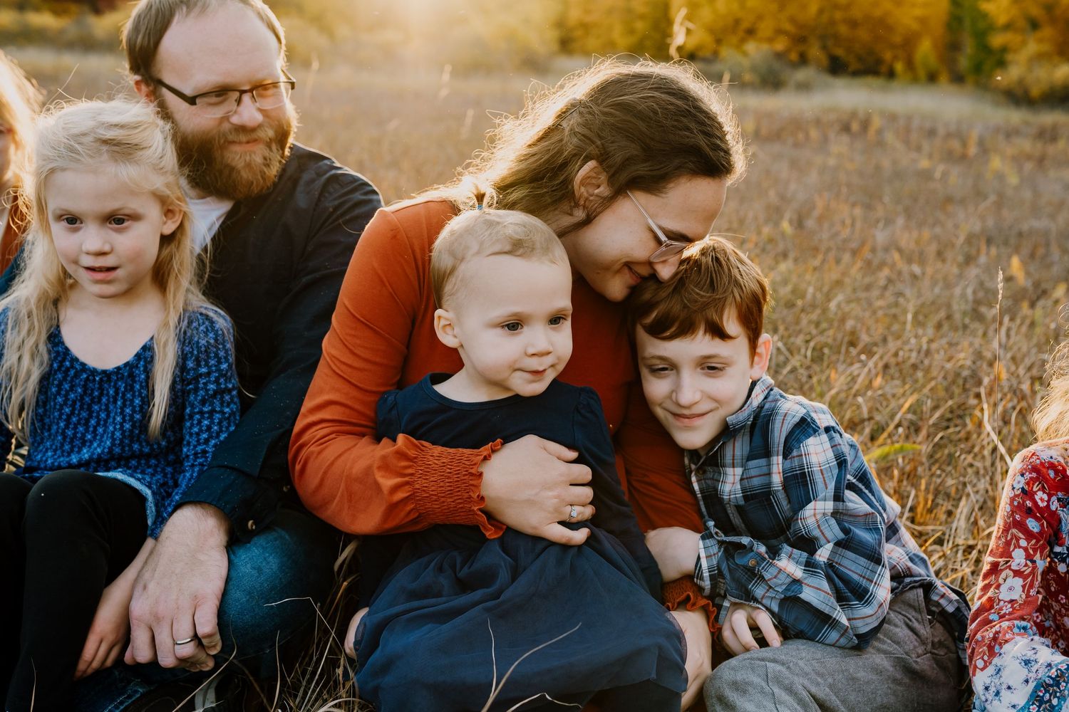 family cuddled in a field at golden hour during family photos with minnesota family photographer