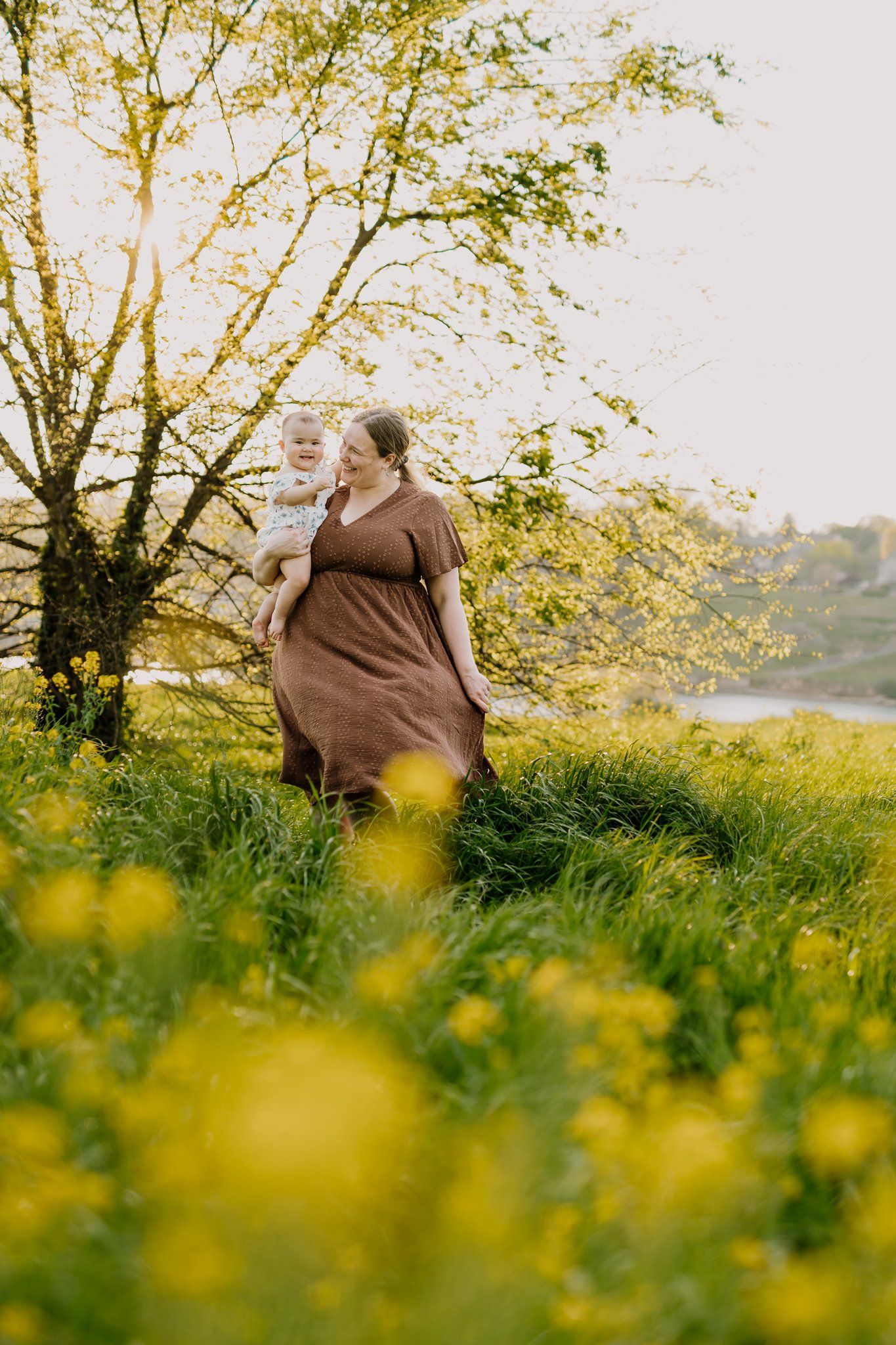 Mom walks through mustard flower field with her baby