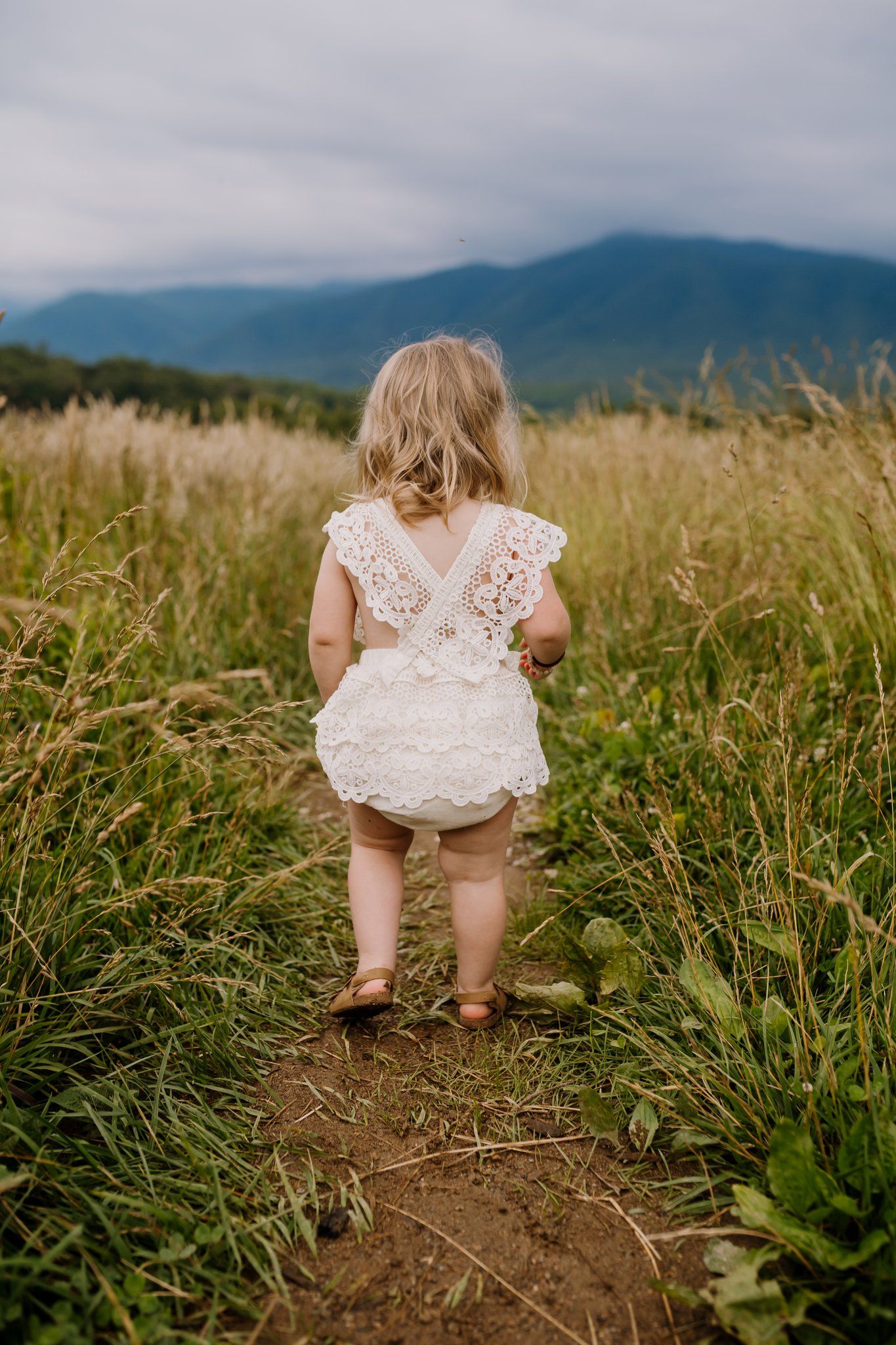 Little girl in ruffle romper stands in field