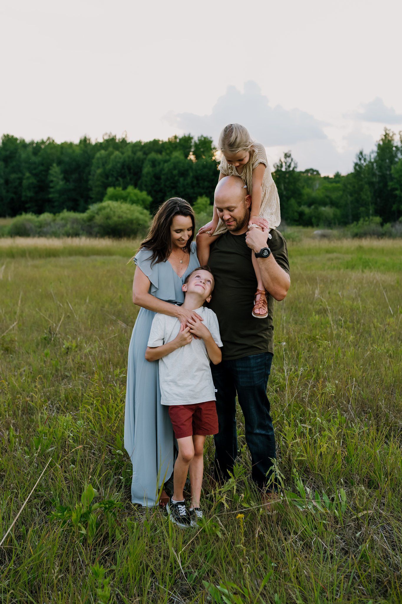 Mom and dad stand in a field with their two kids as they have fun together