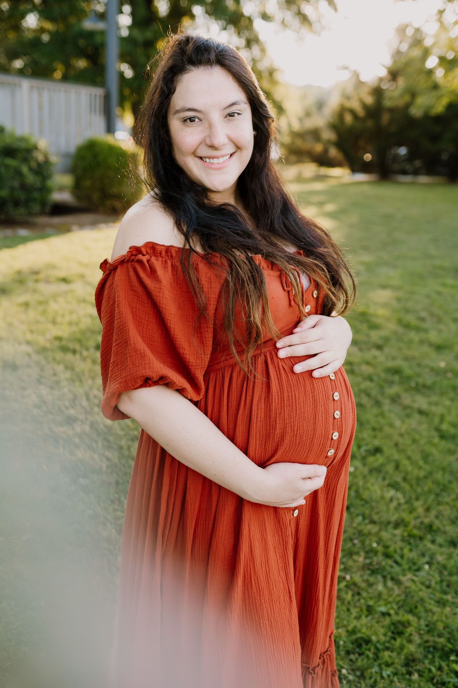 Pregnant woman in a red dress holds her belly and smiles at the camera