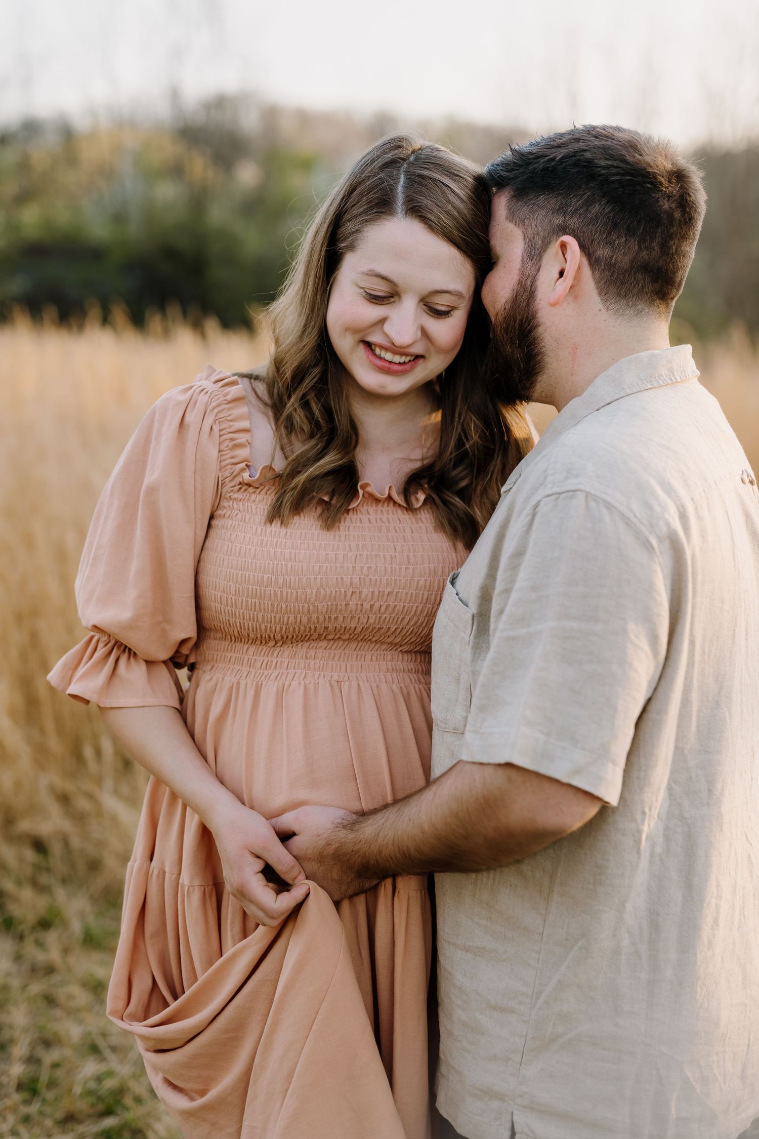 Man embraces and kisses pregnant woman at golden hour in a field