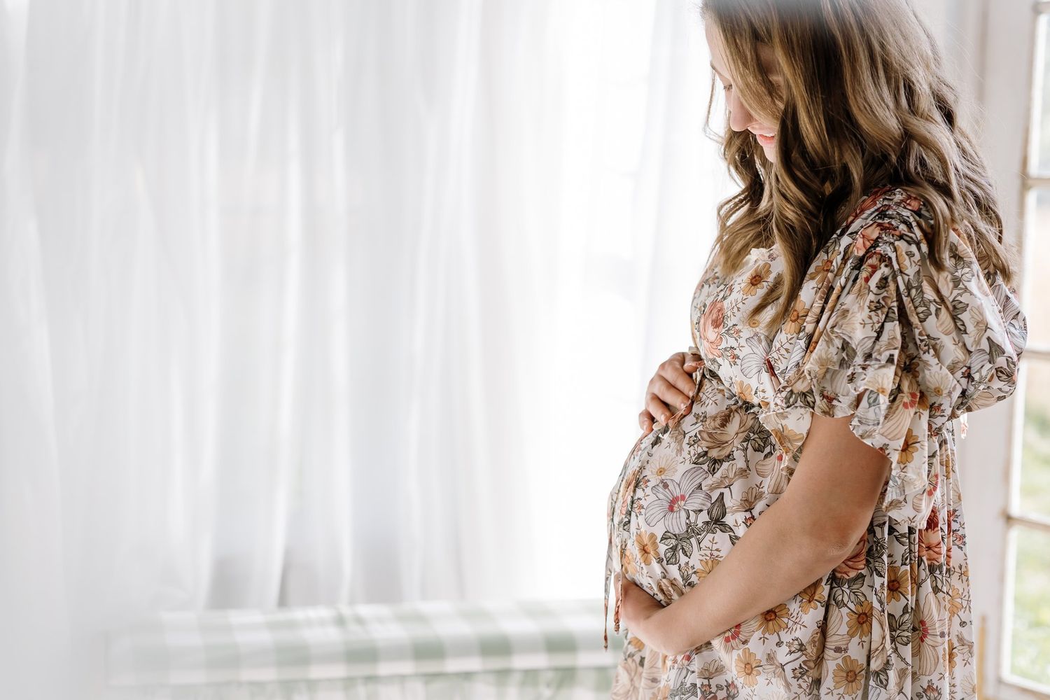 Pregnant woman cradles belly and looks down in the glassholm in karns