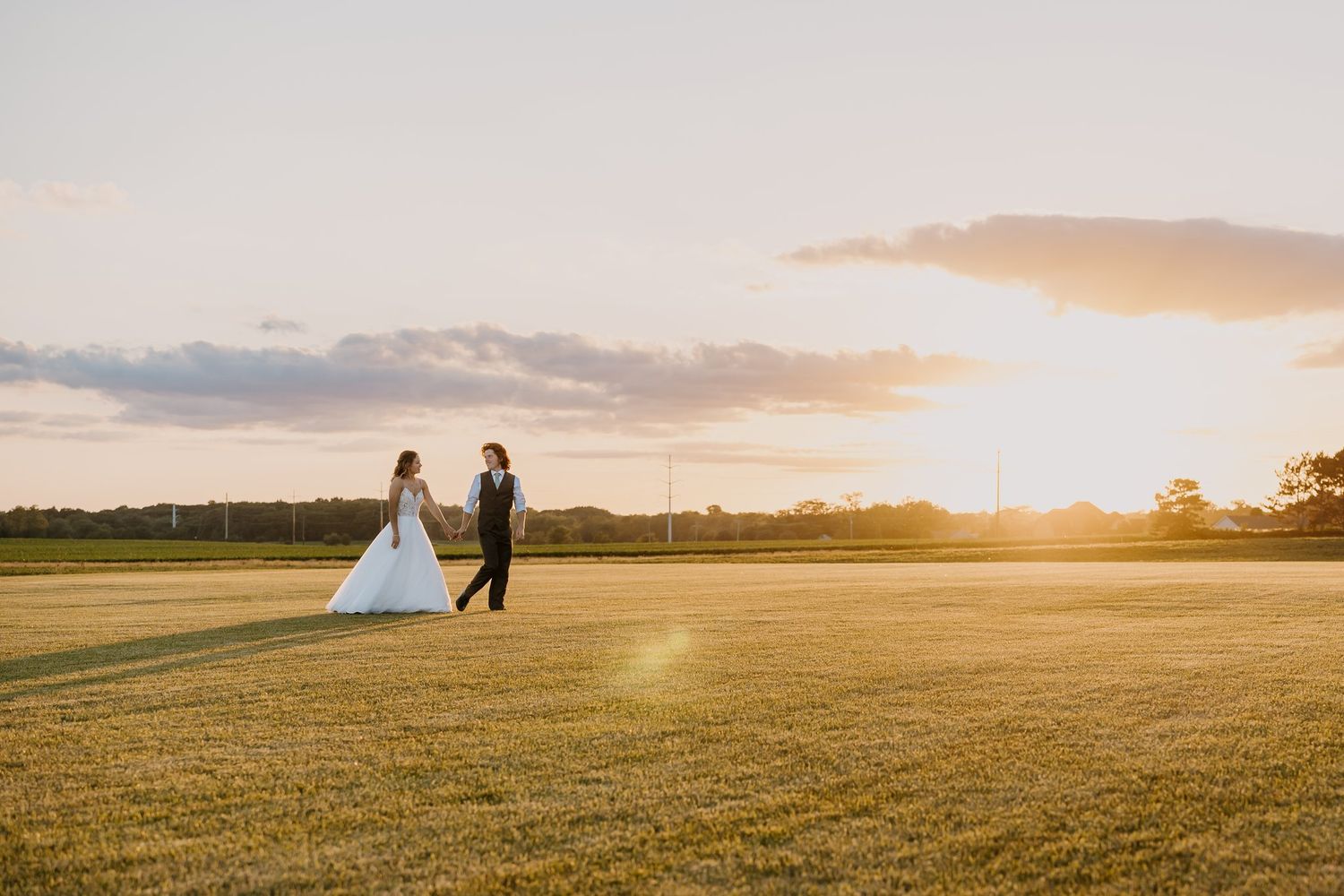 couple walks across grass on their wedding at sunset