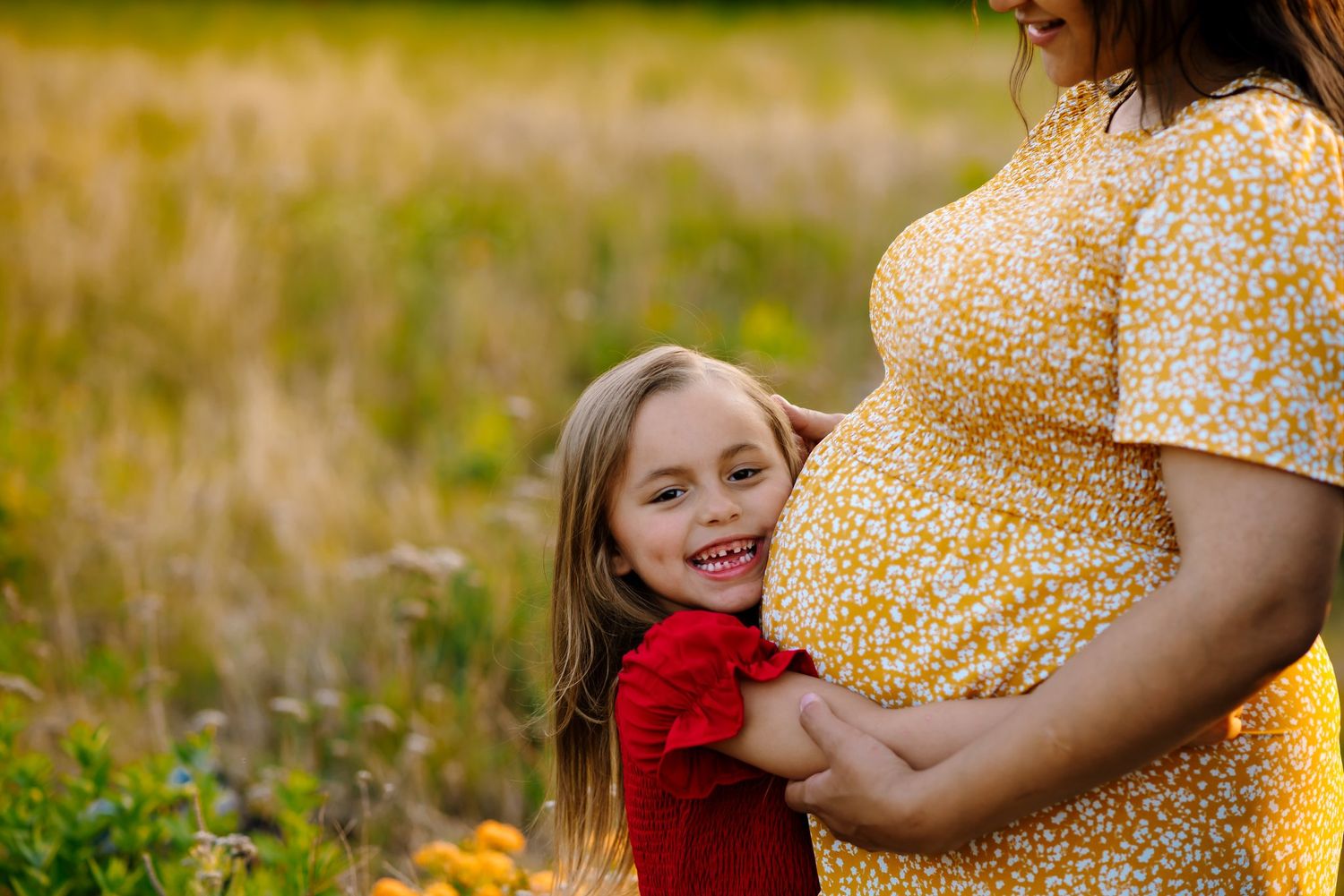 Little girl embraces woman's pregnant belly
