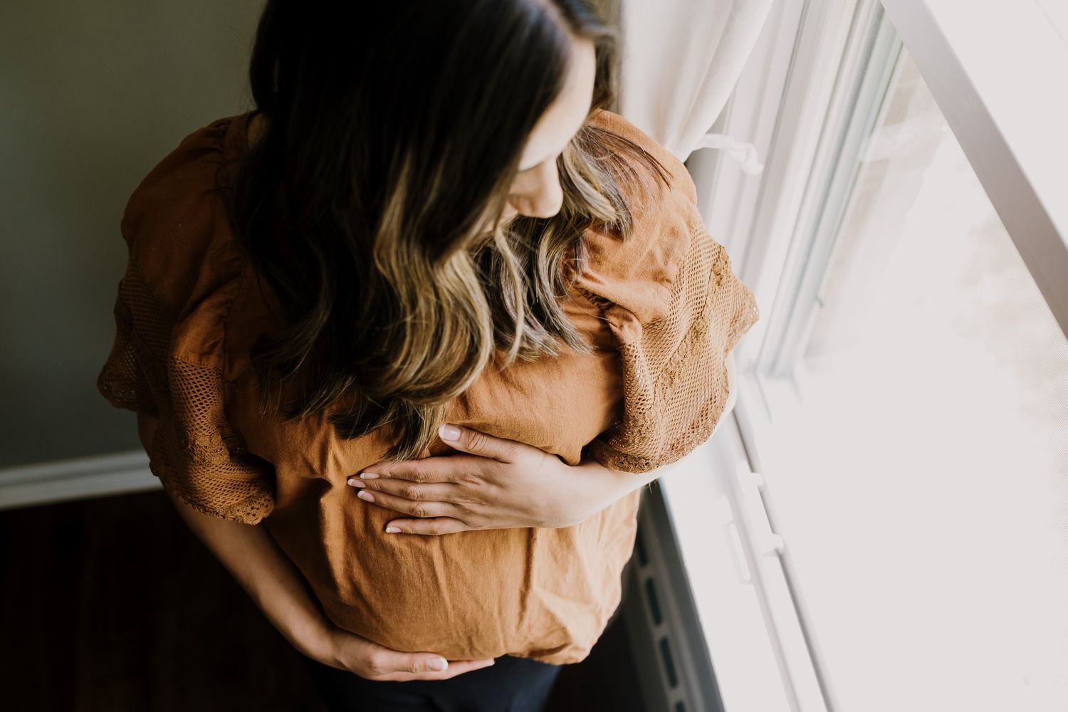 Woman holds pregnant belly and looks out window