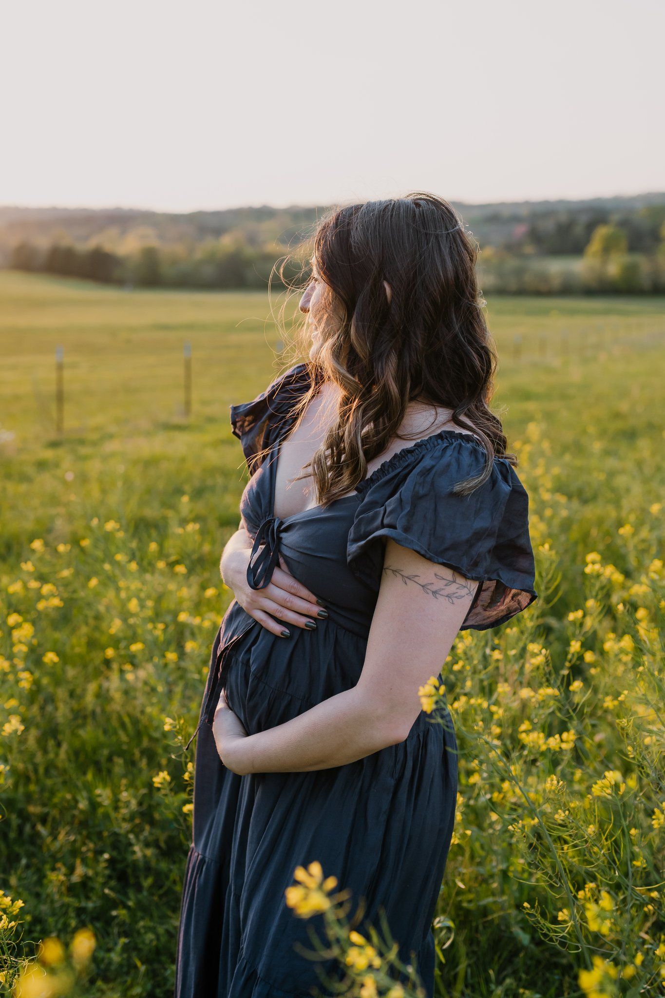 Pregnant mom cradles her belly while standing in a field of yellow flowers