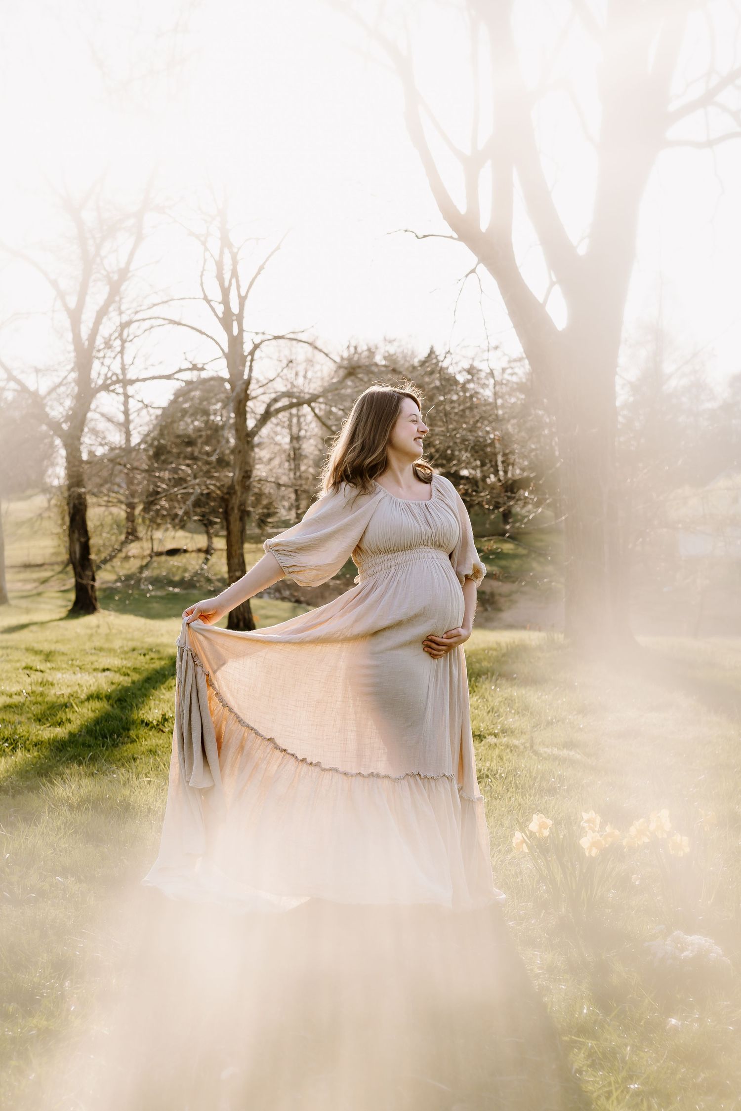 Pregnant woman swishes her skirt and smiles at golden hour