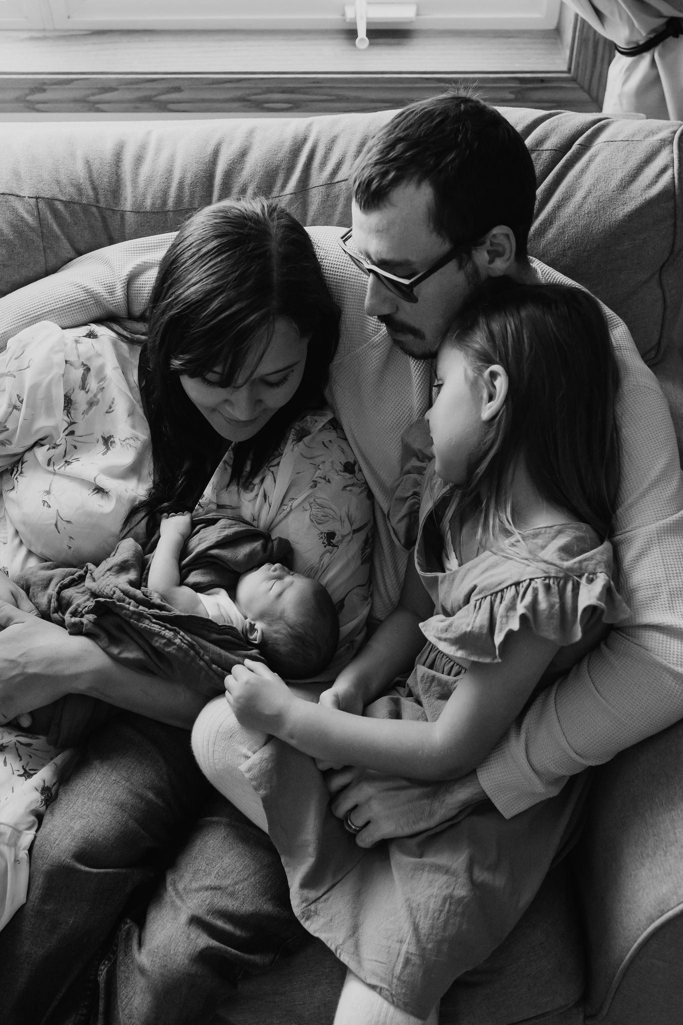 family newborn photo as the family of four sits cozily on their couch in their home