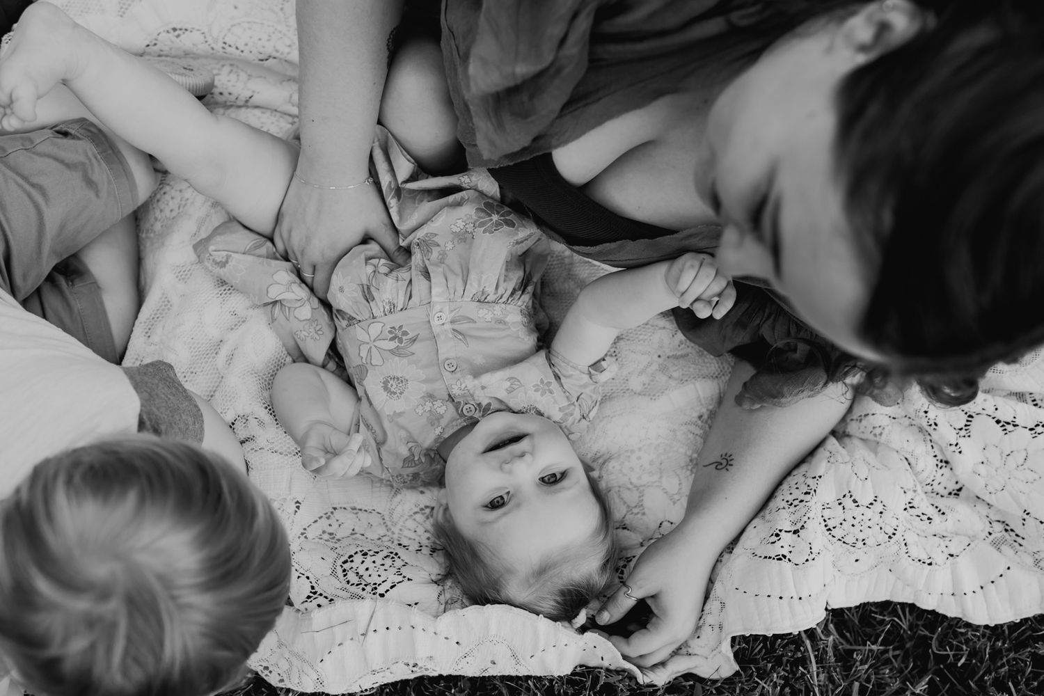Baby lays on blanket next to her mom while her mom holds her hand during summer family pictures