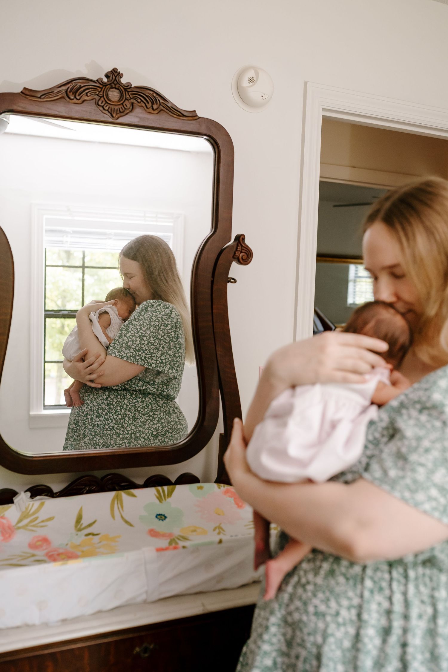 Woman holds her newborn while standing in front of her mirror