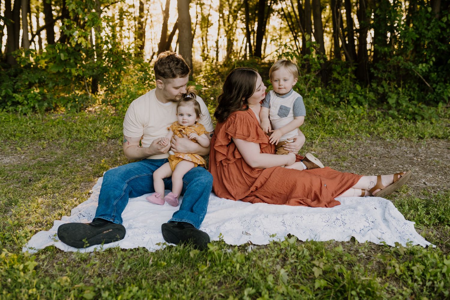 family of four sits in the sunshine during sunshine family pictures outdoors