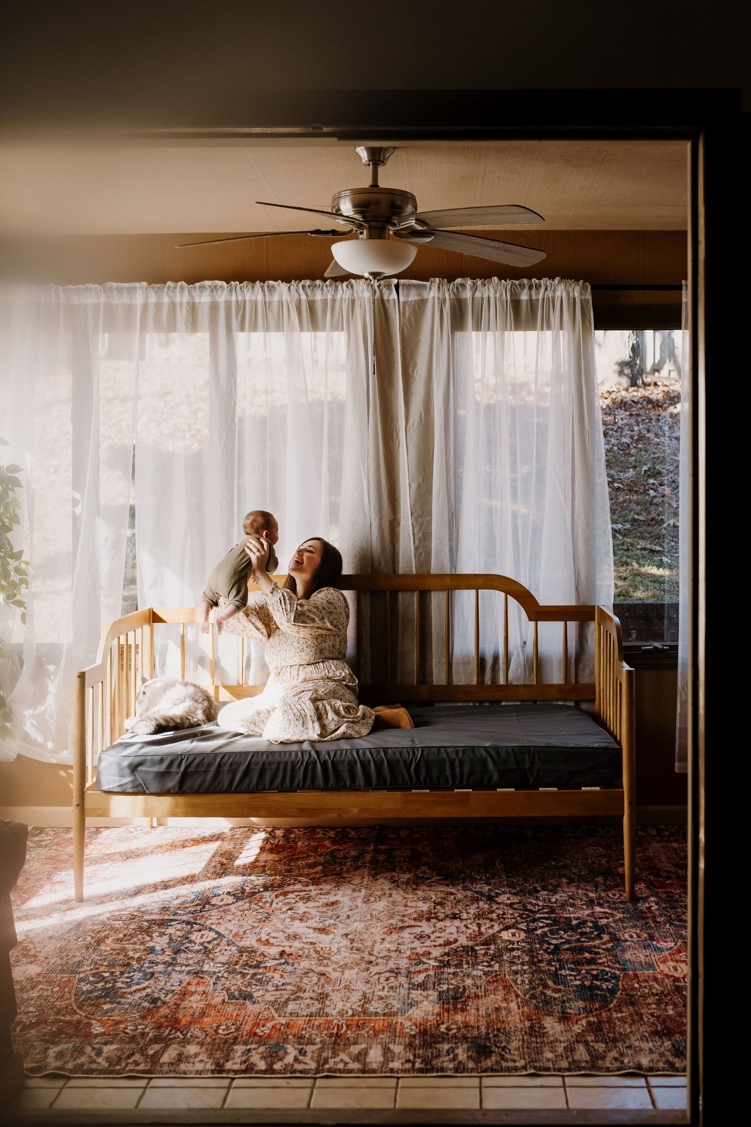 Woman sits on a daybed in their home and plays with her newborn