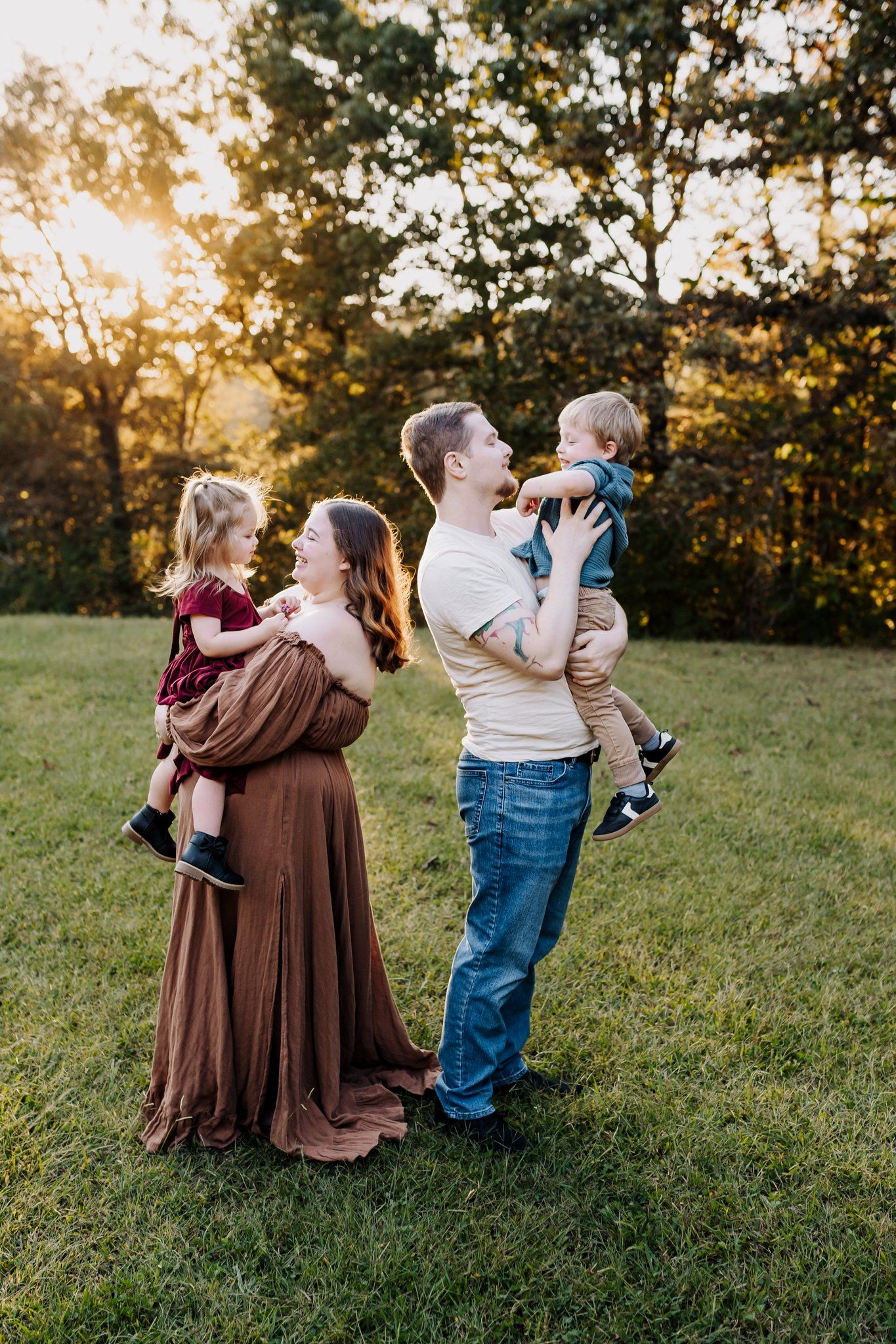 Parents stand back to back holding toddlers at golden hour and playing with them
