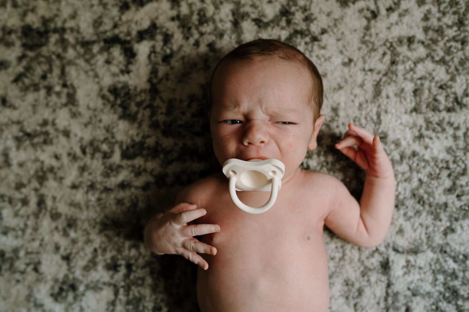 Newborn baby during lifestyle newborn photos grimaces with pacifier in his mouth