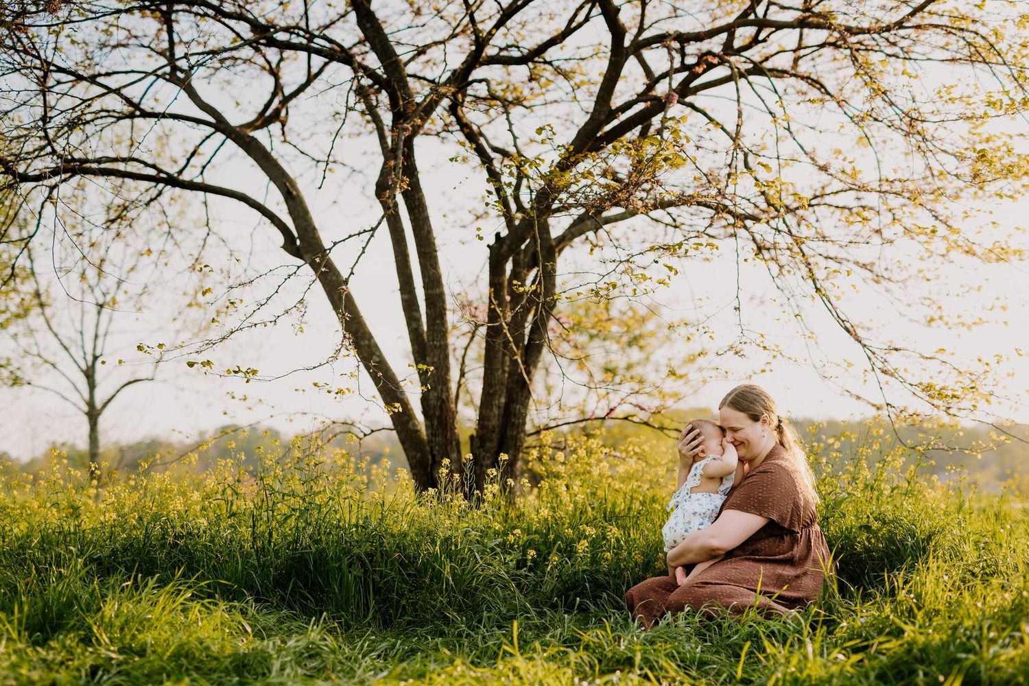 Mom sits in flower field and snuggles her baby during mommy and me mini session knoxville tn