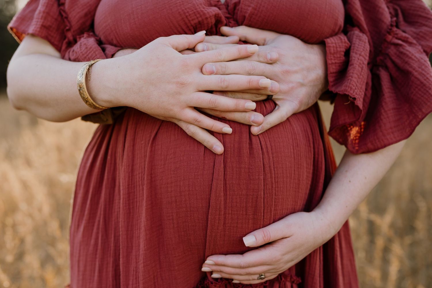 Husband embraces pregnant woman from behind and photo is  of their hands on her belly