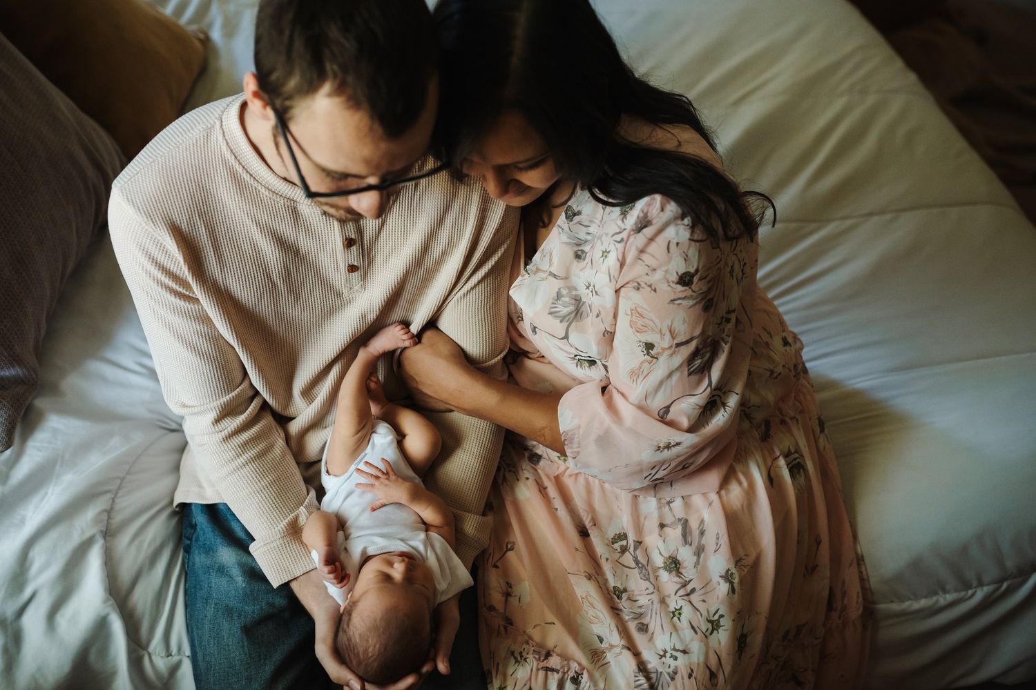 Parents sit on bed and look at newborn