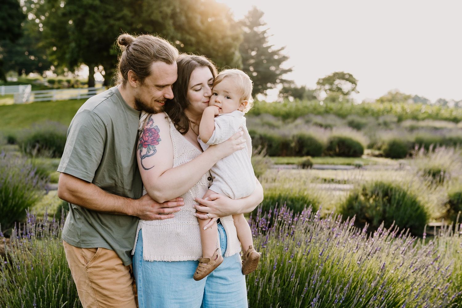 A young family with a baby poses in a lavender field at golden hour, sharing a tender moment outdoors.