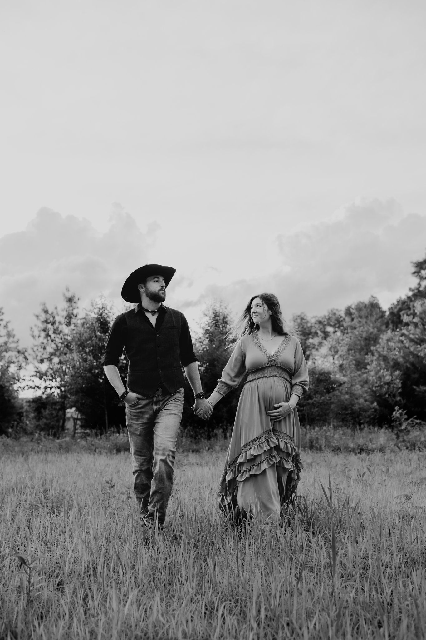 Pregnant woman walks through field holding her husband's hand