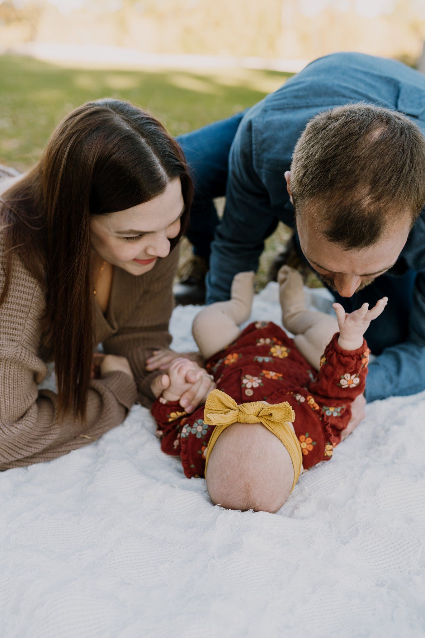 Mom and dad play with baby girl outside on a blanket