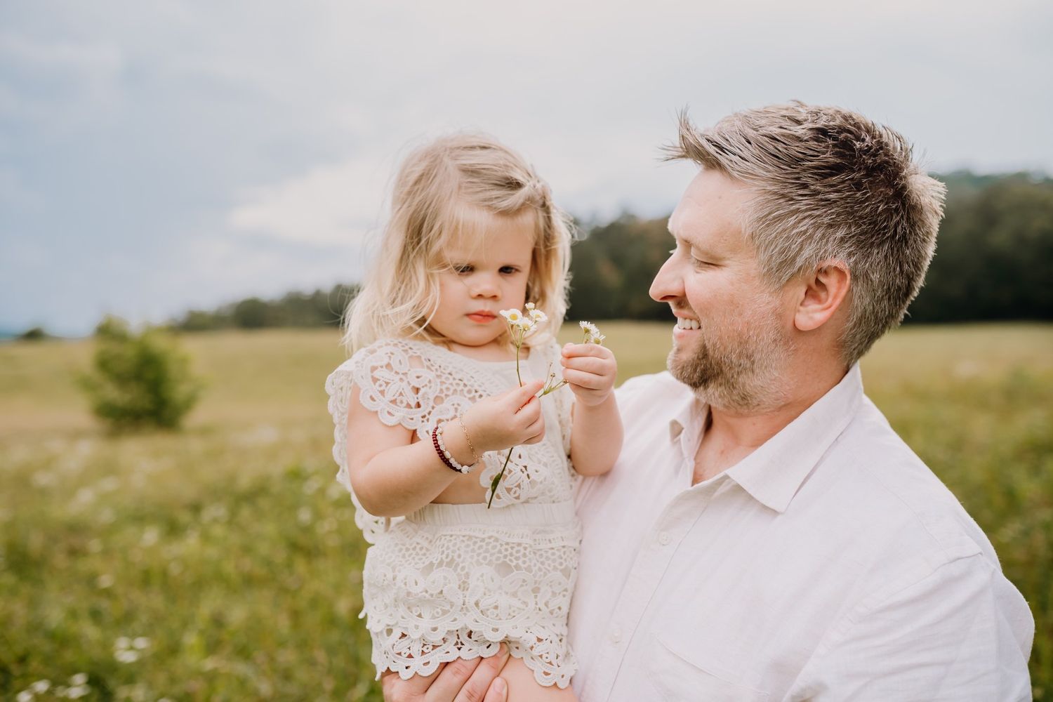 Dad smiles at his toddler as she plays with a flower