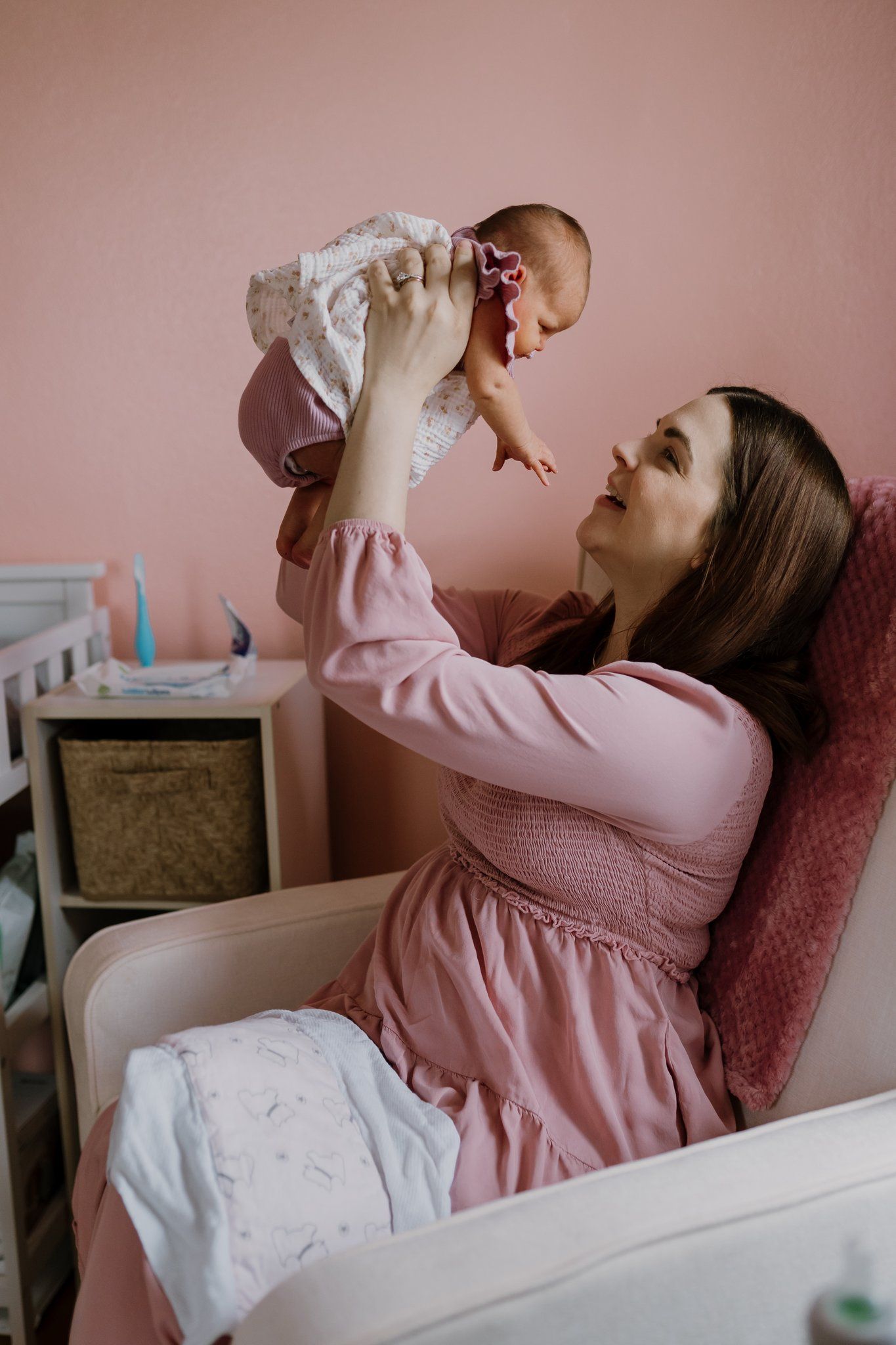 Mom holds newborn up and smiles while sitting in her rocking chair
