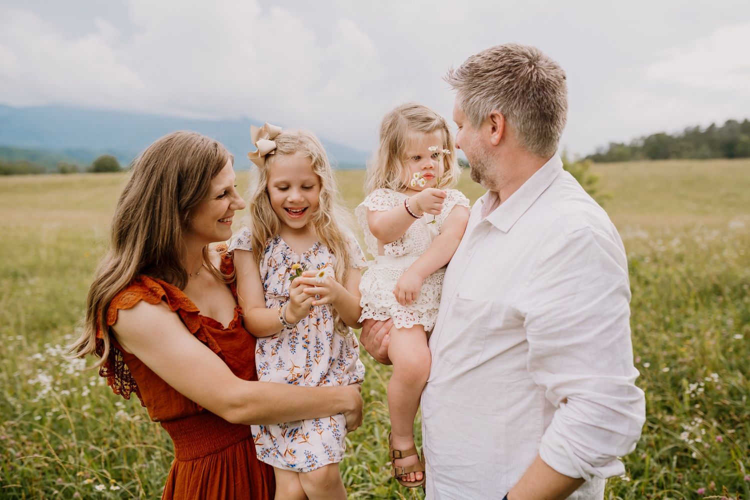 Parents stand side by side each holding a daughter as the girls show them the flowers that they picked