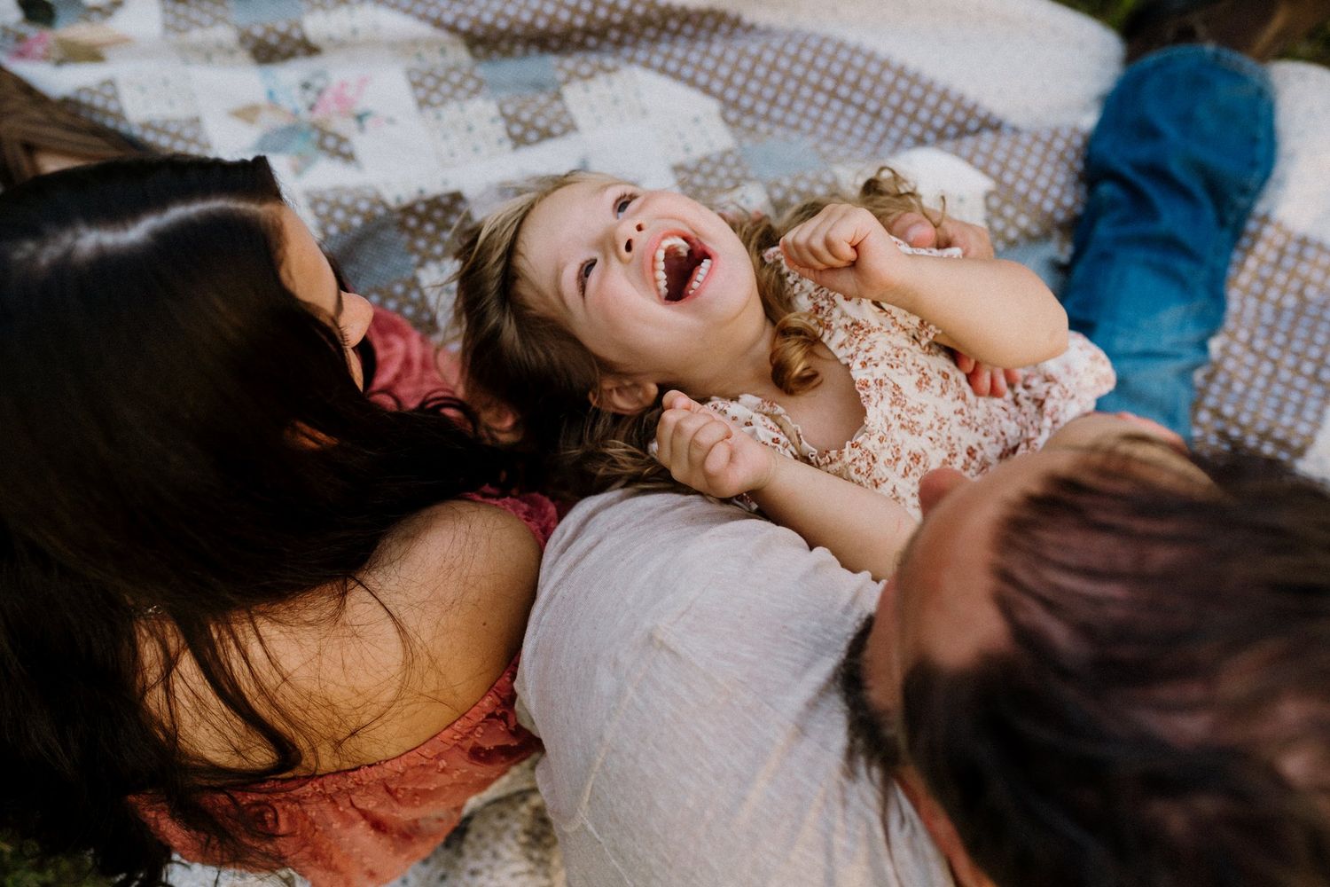 Family laughing together while lying on a picnic blanket outdoors.