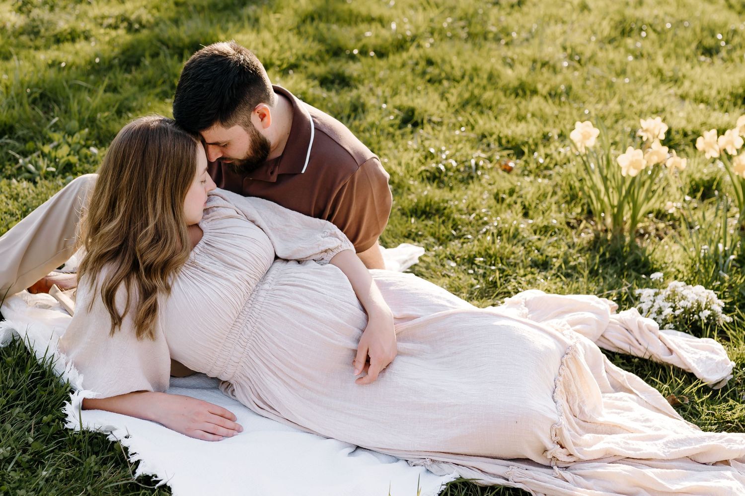 Pregnant woman and her husband lay on the ground and rest foreheads