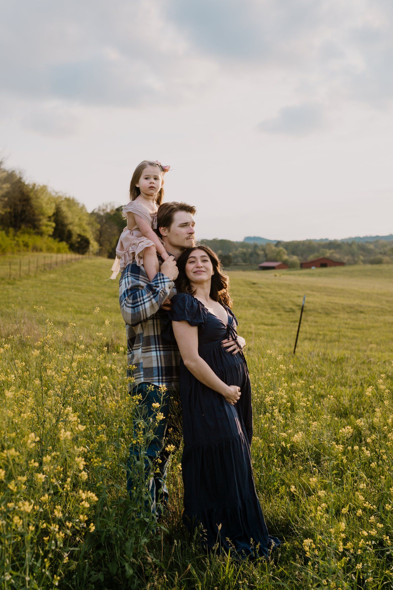 Young family stands together in a mustard field during maternity photo shoot